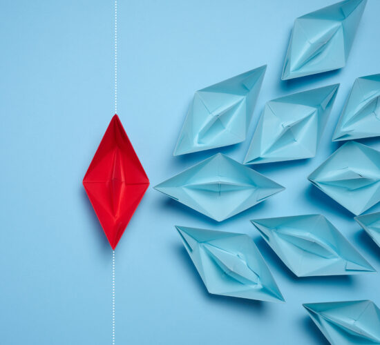 A group of blue paper boats and one red sailing against the current, concept of independent personality, breaking free from influence, strong leadership